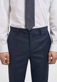 Navy tailored trousers with a smooth texture, slight sheen, belt loops, and front creases; paired with a textured blue tie and white shirt.