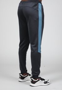 Heren joggers in donkergrijs met een contrasterende lichtblauwe zijkant, voorzien van een getailleerde pasvorm en elastische tailleband. Sneakers met rubberen zool.