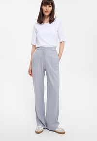 Grijs wijde been broek met hoge taille, gemaakt van een gestructureerde stof met uitgesproken naaddetails, gecombineerd met een eenvoudige witte top met korte mouwen.