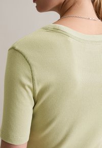 Lichtgroen geribbeld shirt met korte mouwen en een ronde halslijn, met subtiele textuur en stikseldetails langs de naden.