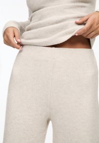 Ensemble de vêtements d'intérieur en maille beige comprenant un haut à manches longues avec des poignets retroussés et un pantalon taille haute, moulant, à la texture douce.