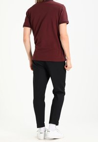 Viininpunainen lyhythihainen poolopaita, jossa kontrastivärinen reunus, yhdistetty mustiin housuihin ja valkoisiin tennareihin, joissa on brändäys kantapäässä.