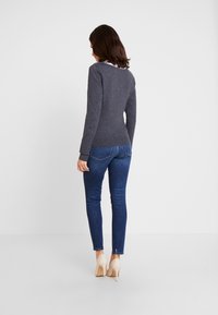 Grå långärmad topp med rund halsringning, kombinerad med mörkblå tajta jeans och beige högklackade skor. Mjuk textur, figurnära design.