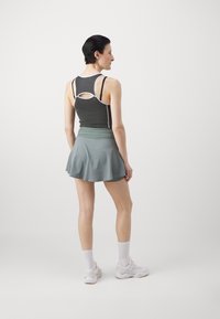 Sports outfit featuring a dark gray tank with white accents and a cutout back, paired with a light green flared skirt.