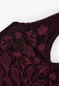 Bordeaux fluwelen stof met ingewikkelde bloemenborduursels in roze en gouden accenten, wat een textuurvolle, elegante uitstraling toont.