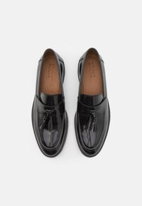 Zwarte lakleren loafers met een gladde afwerking, decoratieve kwastjes aan de voorkant en een contrasterende bruine leren binnenzool. Rondvormig.