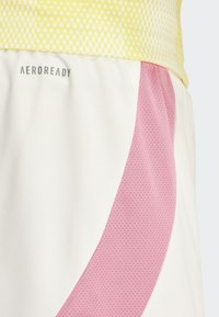 Urheilushortsit, joissa on vaaleankeltainen yläosa ruutukuviolla, valkoinen alaosa ja teksturoitu vaaleanpunainen designkorostus. AEROREADY-logon näkyvä.