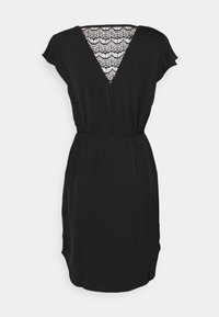 Zwarte jurk met korte mouwen, V-hals, met kantafwerking op de rug. Vloeiende stof met een elastische taille en zijzakken.