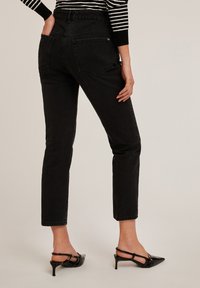 Jeans negros de cintura alta con un corte ajustado, que presentan un diseño clásico de cinco bolsillos y costuras sutiles. Combinados con tacones negros tipo slingback.