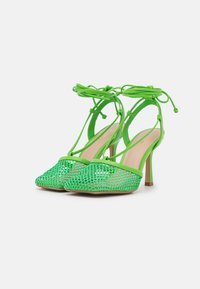 Gröna nät högklackade skor med spetsiga tår, ankelband och en transparent textur. Solida gröna accenter på kanterna och klacken.
