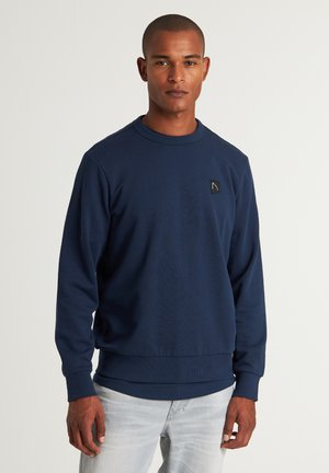 Marineblaues Sweatshirt mit Rundhalsausschnitt, gerippten Bündchen und Saum. Verfügt über ein kleines schwarzes Logopatch auf der Brust. Weicher, strukturierter Stoff.