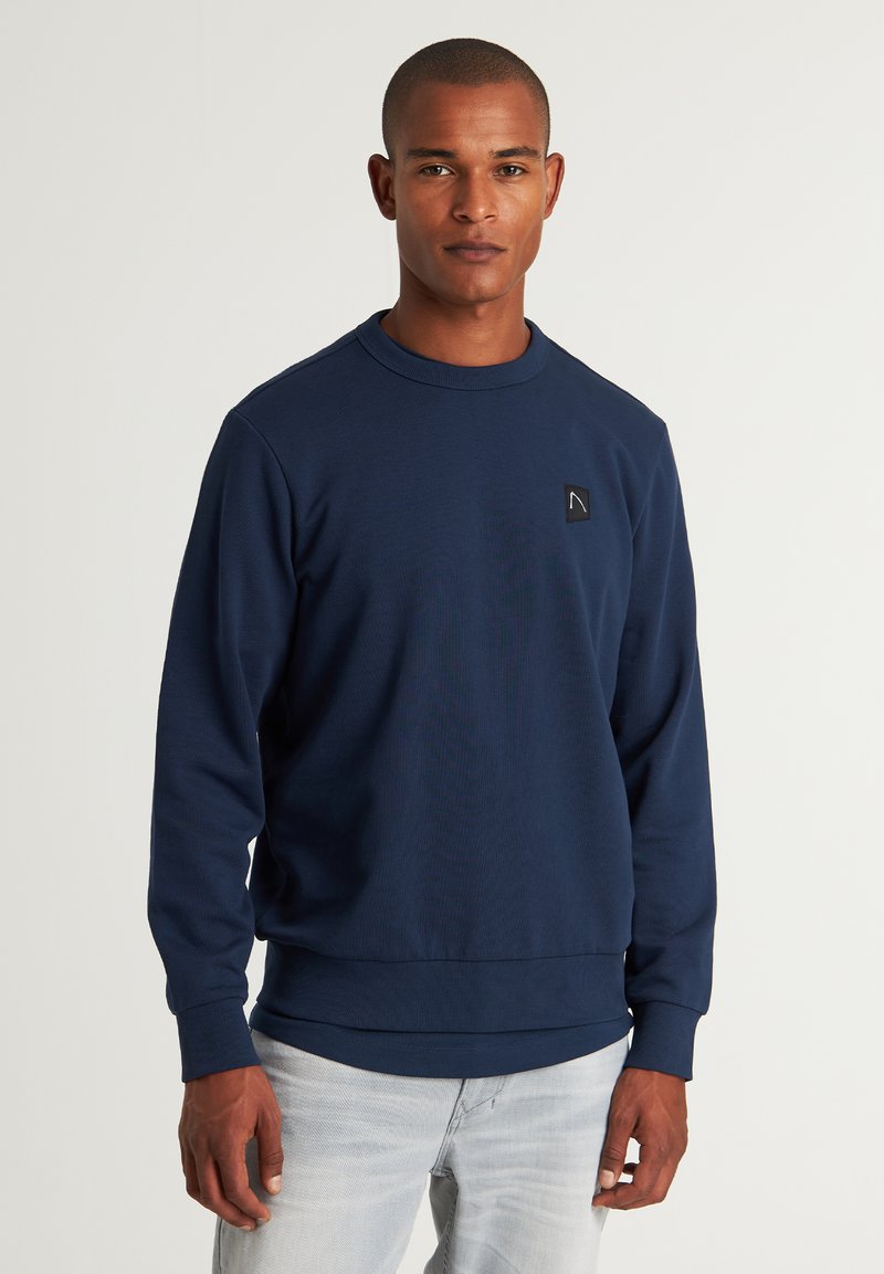 Felpa blu navy con collo a giro, polsini e orlo a costina. Caratterizzata da un piccolo patch logo nero sul petto. Tessuto morbido e strutturato.