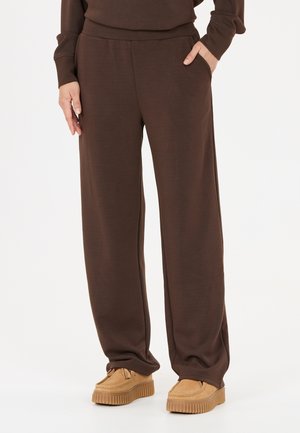 Person wearing loose brown pants with pockets and tan platform shoes against a plain white background.