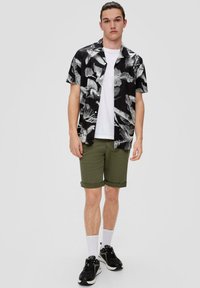 Zwart-wit gestreepte shirt met korte mouwen, witte t-shirt eronder, olijfgroene shorts, zwarte sneakers met witte accenten en witte sokken.