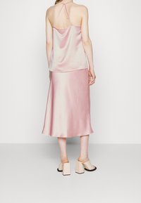 Satin camisole dengan tali yang dapat disesuaikan dipasangkan dengan rok midi berwarna pink lembut, yang memiliki tekstur halus. Mules dengan tumit chunky berwarna beige.