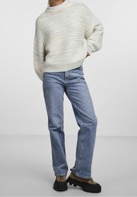 Chunky, ljust färgad stickad tröja med horisontella ränder, tillsammans med blå raka jeans och mörka snörstövlar.