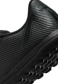 Scarpa sportiva nera con superficie testurizzata, caratterizzata da linee orizzontali e una suola con motivo per la trazione. Branding minimali in colore scuro.