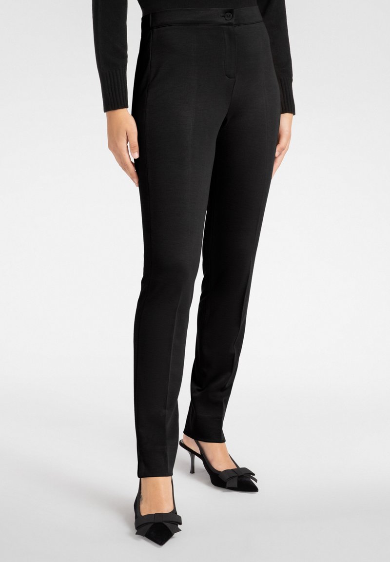 Svarta skräddarsydda byxor med smal passform, med en slät textur, framfickor och knappstängning. Bärs med svarta spetsiga klackar.