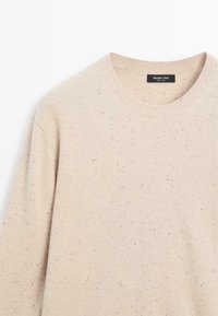 Beżowy sweter dzianinowy z okrągłym dekoltem. Posiada wielokolorowe kropeczki na całej powierzchni materiału. Miękka tekstura i prążkowany detal przy kołnierzu.