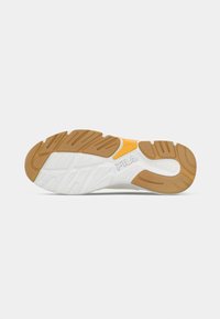 Suela de sneaker blanca y marrón con goma texturada, con un acento amarillo y el logo de Fila, diseñada para tracción y comodidad.