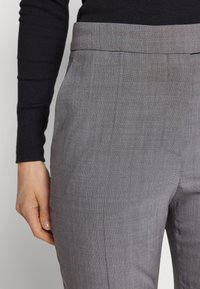Szare spodnie w kant o gładkiej teksturze i subtelnym wzorze w kratkę. Mają płaski przód i boczne kieszenie, zaprojektowane z myślą o dopasowanym fasonie.
