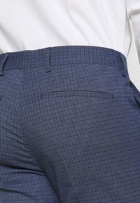 Navy blue checked trousers with a straight cut. Notable details include a back pocket and a smooth texture.