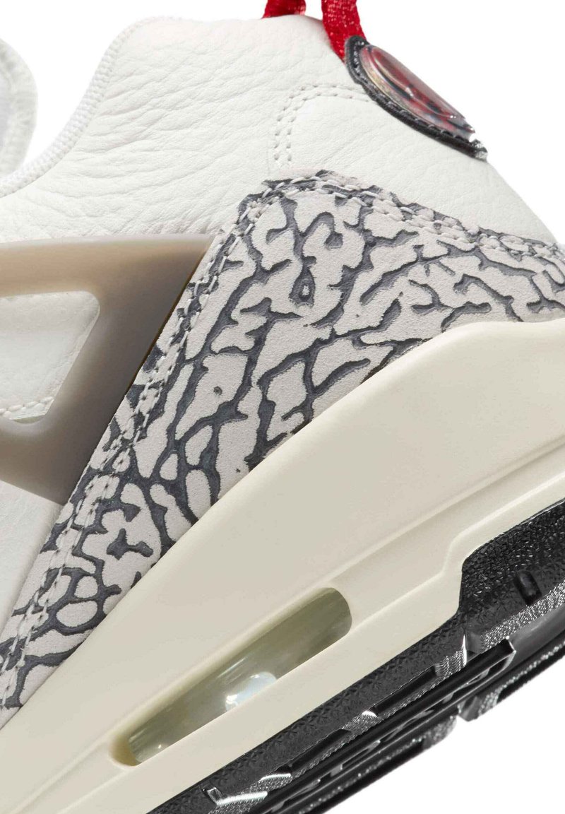 Zapatilla de cuero blanca con acentos texturizados en gris, almohadilla de aire transparente y tirador rojo. Suela de goma negra con patrón de relieve detallado.