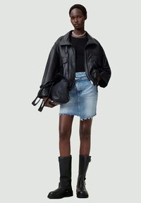 Donna con giacca di pelle nera, top nero, gonna di jeans azzurri, stivali neri, collana in argento, mentre tiene una borsa nera.