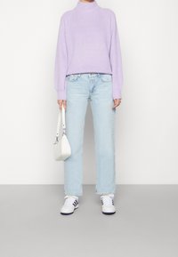 Pull en tricot lavande avec col montant, jean bleu clair à jambes droites, sac à main blanc et baskets blanches avec des accents violets.