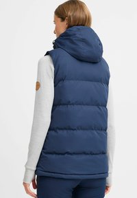 Gilet matelassé bleu marine avec capuche, présentant un design matelassé et une patch logo sur l'épaule. Tissu doux avec une texture lisse.
