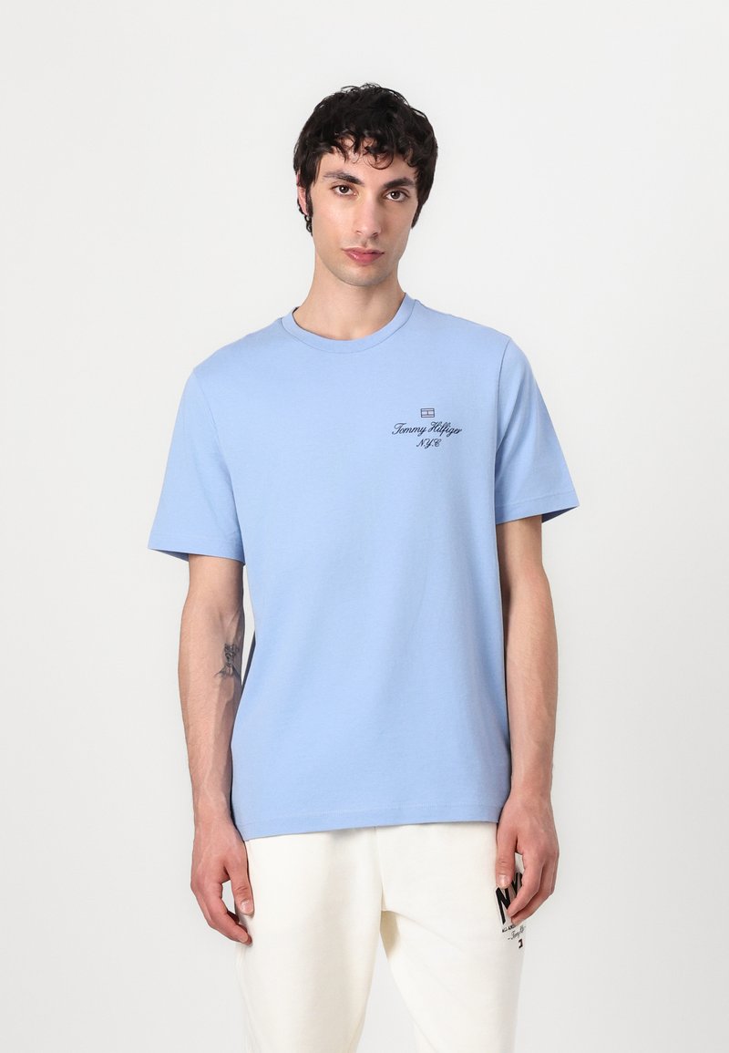 T-shirt en coton bleu clair à manches courtes, col rond et petit logo noir imprimé sur la poitrine. Texture douce et coupe décontractée.