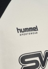 Prim-plan cu o țesătură albă cu logo-ul negru "hummel SPORTSWEAR" și un design grafic parțial alb-negru.