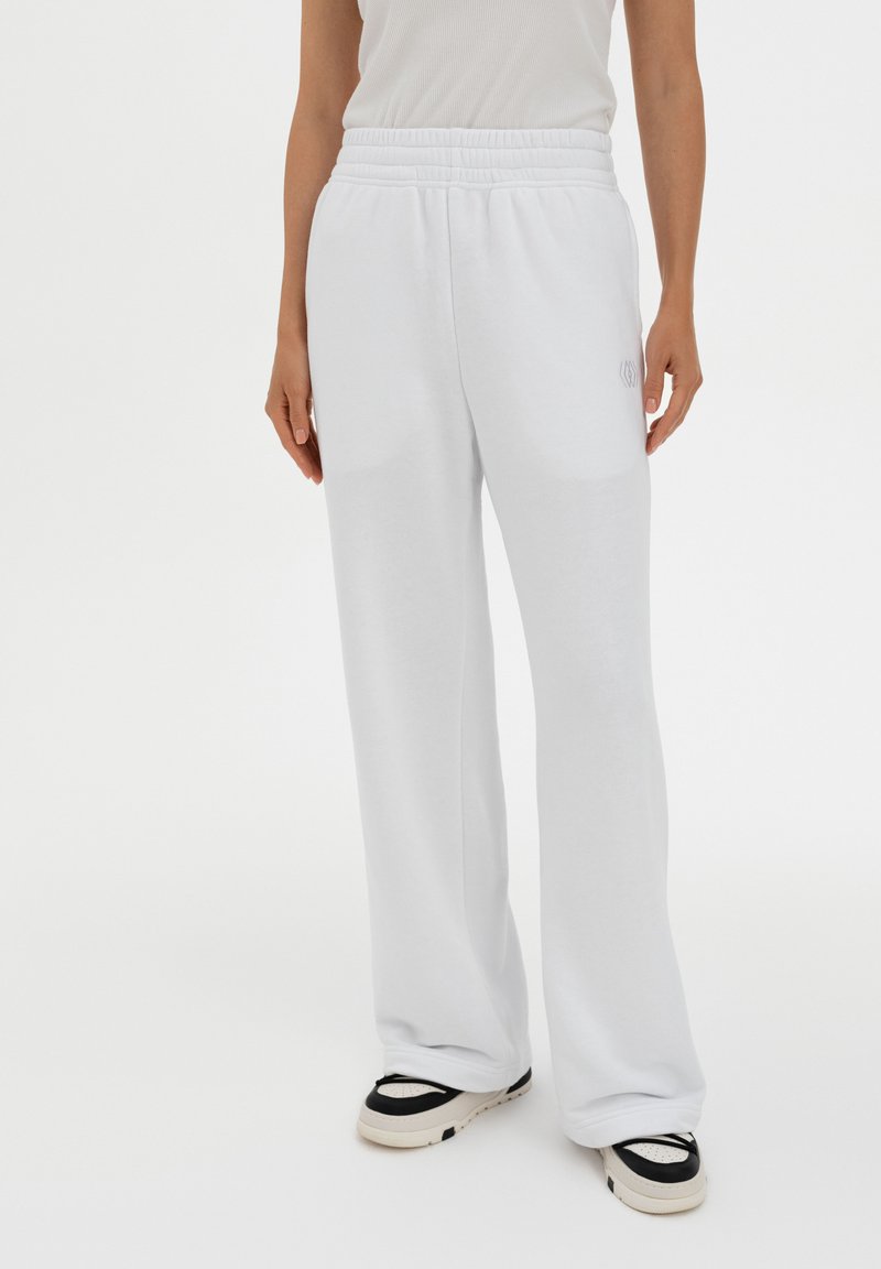 White, loose-fitting sweatpants made of soft fabric. Features an elastic waistband and a subtle logo detail on the side.