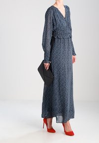 Długa niebieska sukienka w kwiaty o kroju kopertowym, z marszczonym stanikiem i długimi rękawami. Połączona z czarną kopertówką i czerwonymi szpilkami.