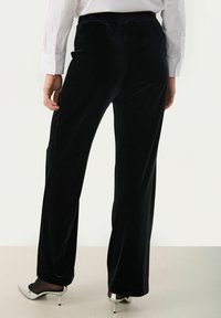 Pantaloni negri din catifea cu un design cu picior drept, având o textură netedă și un talie înaltă, asortați cu tocuri albe ascuțite.