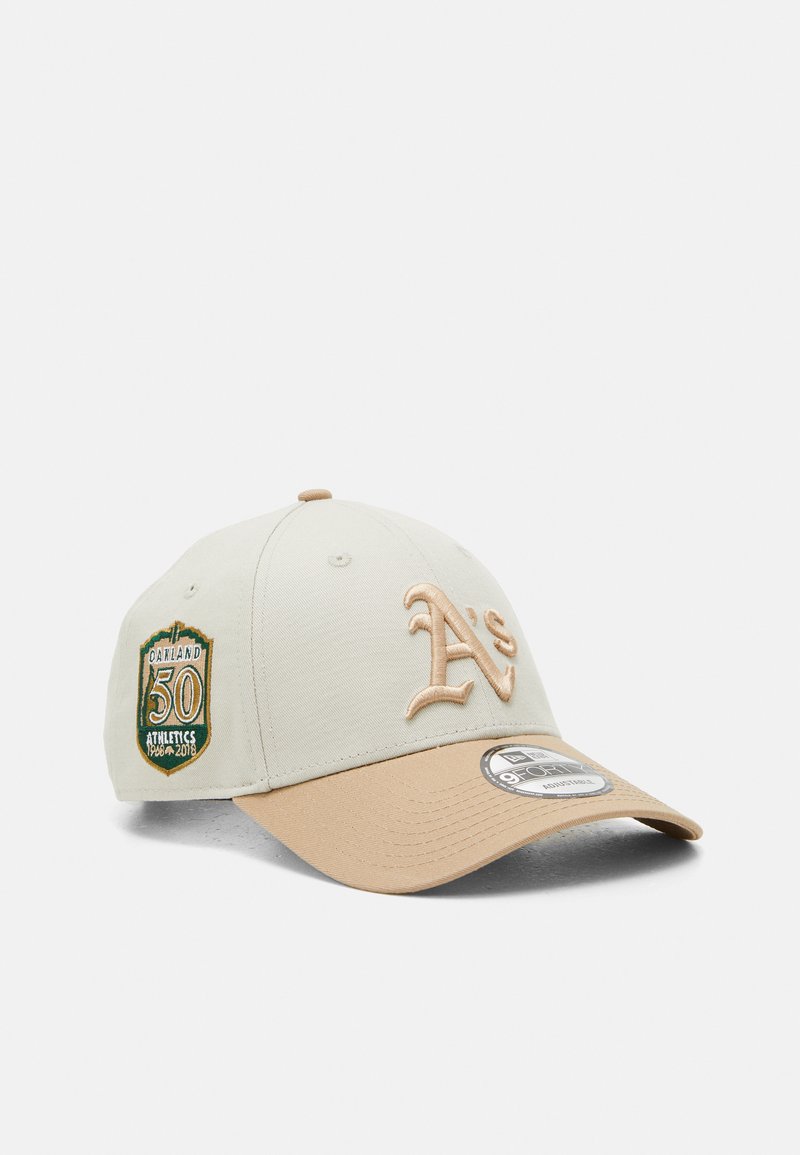 Casquette beige avec une visière bronzée, arborant un logo "A's" brodé et un patch vert et or indiquant "Oakland 50 Athletics 1968-2018."