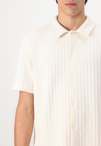 Kortärmad knapp-up skjorta i off-white. Vaffeltextur, mjukt tyg, strukturerad krage och fem framknappar.