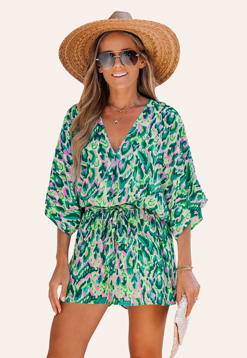 Kleurrijke groene en roze luipaardprint romper met een V-hals, korte mouwen en een strik taille. Model houdt een clutch vast en draagt een strooien hoed.