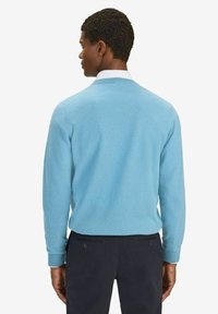 Ljusblå, långärmad tröja i mjukt tyg, med ribbade ärmslut och rund halsringning, buren över mörka byxor.