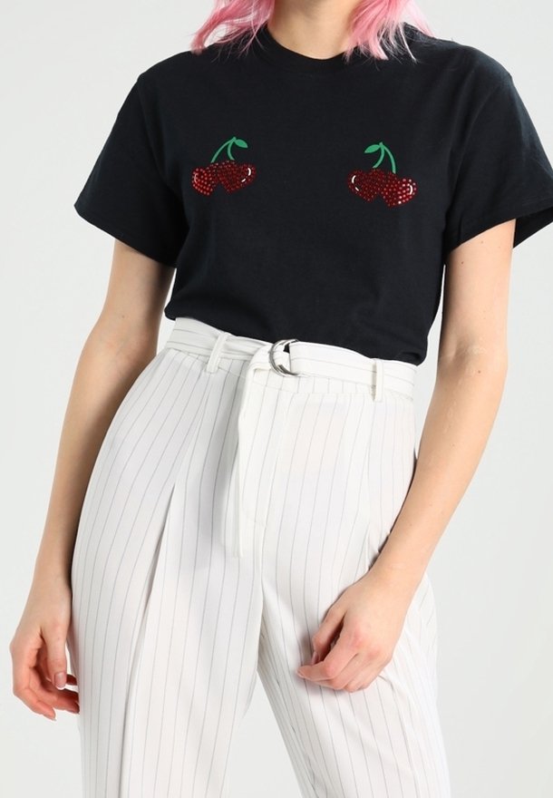 Svart bomullströja med röda körsbärsapplikationer på bröstet; kombinerad med höga vita randiga byxor och ett bälte.