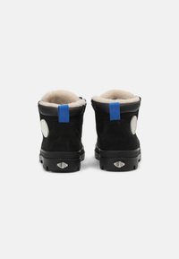 Botas de tornozelo em camurça preta com um acabamento texturizado, apresentando remendos de logótipos brancos e alças do calcanhar azuis, forro suave em bege e solas de borracha.