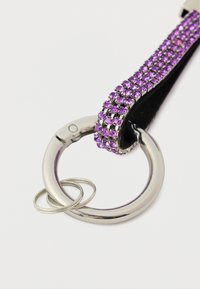 Lillaest litritega kaetud võtmehoidja metallist rõnga ja hõbedase aktsendiga, millel on tekstureeritud rihm sileda nahast tagapinnaga.