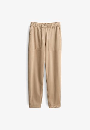 Beige Hosen aus weichem Stoff, mit einem breiten elastischen Bund, zwei Fronttaschen und schmal zulaufenden Beinen. Glatte Textur und minimales Design.
