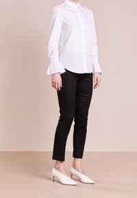 Witte blouse met uitlopende mouwen, gecombineerd met zwarte slim-fit broek en witte puntige hakken met een kleine hak.