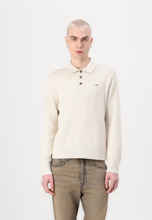 Cremefarvet langærmet polo skjorte med knaplukning, rib-strikkede manchetter og et lille logo på venstre bryst. Stylet med lyse denim jeans.