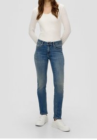 Fitted blue jeans with a slight fade, five-pocket design, and belt loops, paired with a white long-sleeve top and white sneakers.