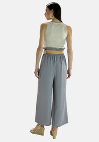 Pantalons larges gris clair avec une taille élastique à volants, associés à un haut sans manches beige et accessoirisés avec une ceinture tissée.