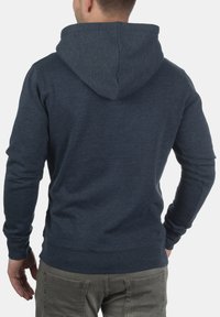 Navyblauer Kapuzenpullover mit glatter Textur, engen Bündchen und einer Kängurutasche. Sichtbare Nähte entlang der Nähte.
