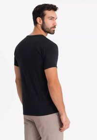 Czarna koszulka z krótkim rękawem, okrągłym dekoltem, dopasowanym krojem i gładką fakturą, widoczna z tyłu na białym tle.