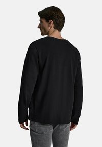 Czarna bawełniana koszula z długim rękawem o luźnym kroju, okrągłym dekolcie i prostym wykończeniu. Wydaje się miękka, z minimalną ilością szwów.